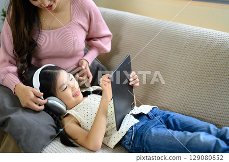 Mom and little girl enjoying technology together in a cozy living room 129080852