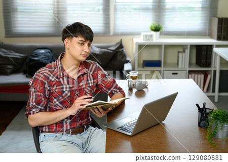 Young caucasian man taking notes during online learning session Young caucasian man taking notes during online learning session 129080881