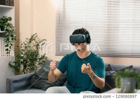 Male gamer playing immersive VR racing game while sitting on a sofa 129080897