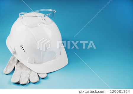White construction worker safety helmet with personal protective equipment on blue background White construction worker safety helmet with personal protective equipment on blue background 129081564