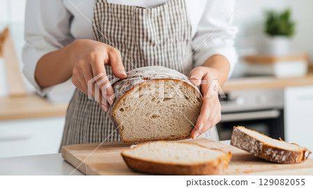 Female hands slicing fresh bread on wooden cutting board in kitchen 129082055
