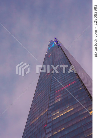 The Shard in London is captured from a low angle, highlighting its height and modern design. Subtle lighting and a dusky sky enhance the glass facade. 129082992