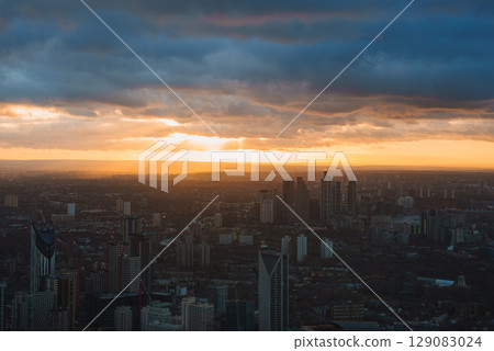 View of London's skyline during sunset, featuring prominent skyscrapers and modern buildings under a sky filled with dramatic clouds. 129083024