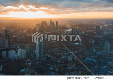The image shows an aerial view of London's skyline at sunset, featuring modern skyscrapers, iconic buildings, and the River Thames under a warm sky. The image shows an aerial view of London's skyline at sunset, featuring modern skyscrapers, iconic buildings, and the River Thames under a warm sky. 129083028