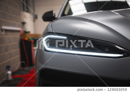 Close up view of the Lamborghini Urus front left headlight with angular LED design, matte silver finish, and red carpet in a garage or showroom. 129083059