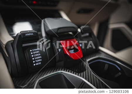 Detailed view of the Lamborghini Urus center console featuring a red engine start button, driving mode controls, and beige interior elements. 129083106