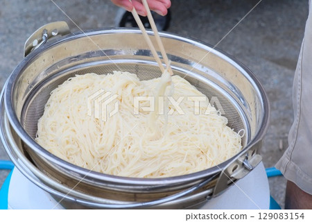 Picking up somen noodles from a strainer with chopsticks 129083154