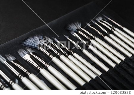 Paint tubes, brushes for painting and palette knifes on old wooden background 129083828