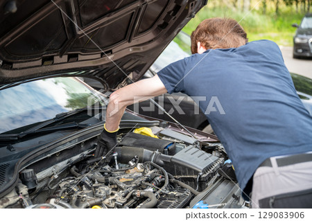 Man repairing car engine in residential outdoor parking area on a sunny summer day 129083906