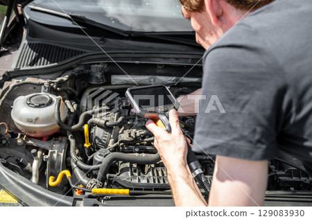 Mechanic using diagnostic tool to inspect car engine during vehicle maintenance 129083930