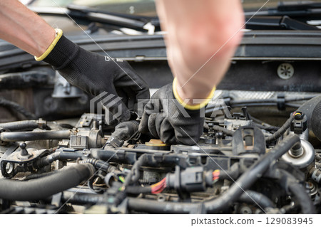 Mechanic wearing gloves fixing engine wiring inside car during repair Mechanic wearing gloves fixing engine wiring inside car during repair 129083945
