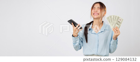 Happy Asian woman showing phone and holding money fan, online shopping winner excited about finance, money success from mobile rewards and digital transaction power. isolated studio white background 129084132