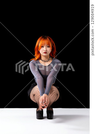 Asian Woman With Orange Hair Squats in Studio Against Black Background 129084919