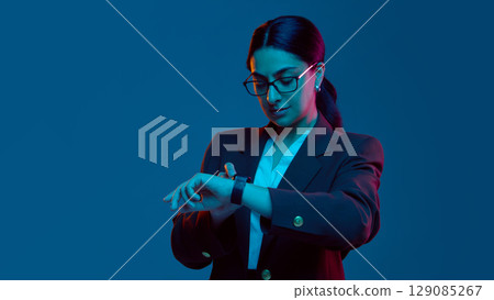 Businesswoman checking smartwatch in blue neon studio Businesswoman checking smartwatch in blue neon studio 129085267