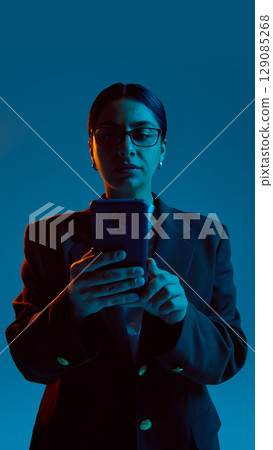 Portrait of serious businesswoman using smartphone under blue lighting Portrait of serious businesswoman using smartphone under blue lighting 129085268