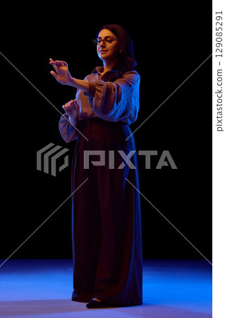 Full-body view of woman using virtual interface in neon light Full-body view of woman using virtual interface in neon light 129085291