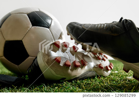 Football cleats resting near ball on green grass with white background 129085299
