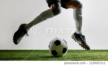 Football player jumping with feet above ball on green turf Football player jumping with feet above ball on green turf 129085312