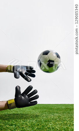 Football goalkeeper hands in gloves reaching for flying ball 129085340