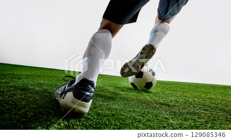 Soccer player dribbling black and white ball on grass field in motion 129085346