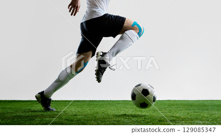 Soccer player running on field with ball wearing white uniform and knee tape Soccer player running on field with ball wearing white uniform and knee tape 129085347