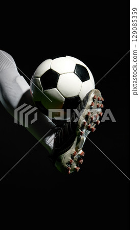 Soccer player lifting ball with foot against black background Soccer player lifting ball with foot against black background 129085359