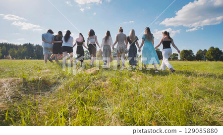 High school students linking arms and strolling through a sunlit field on a summer day, savoring their time together High school students linking arms and strolling through a sunlit field on a summer day, savoring their time together 129085880