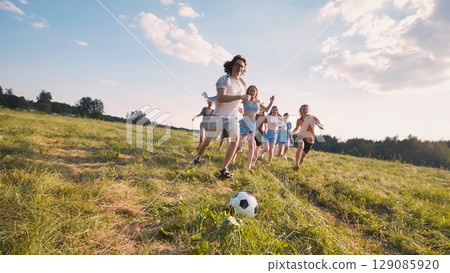 Group of cheerful teenagers running across green meadow on sunny summer day, playing soccer Group of cheerful teenagers running across green meadow on sunny summer day, playing soccer 129085920
