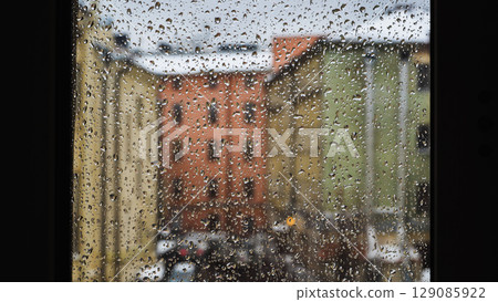 Raindrops sliding on window glass blurring buildings in the background Raindrops sliding on window glass blurring buildings in the background 129085922