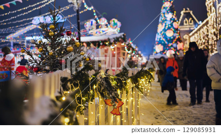 Christmas market glowing at night with decorated fence, christmas tree and people walking 129085931
