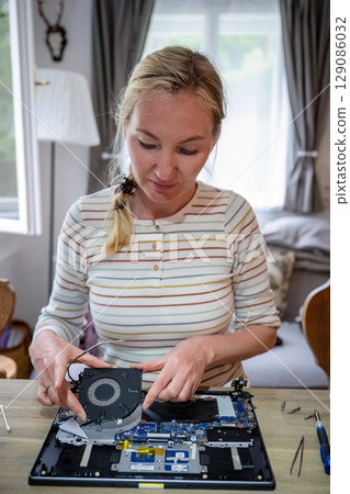 Woman repairing laptop with tools on table, computer maintenance concept 129086032