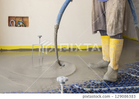 Man pouring concrete over floor heating installation in a new building. Modern construction system Man pouring concrete over floor heating installation in a new building. Modern construction system 129086383