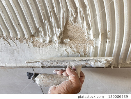 Craftsman spreads wall tile adhesive with trowel a house wall, hand closeup. Construction process 129086389
