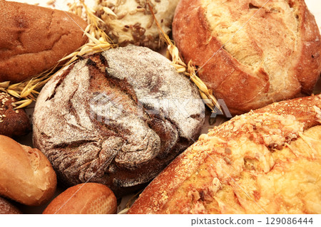 Mix of baked bread varieties on wheat grains background, fresh loafs from bakery on ructic background, selective focus, toned Mix of baked bread varieties on wheat grains background, fresh loafs from bakery on ructic background, selective focus, toned 129086444