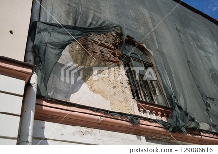 The Decaying Facade of a Building Exhibiting Significant Structural Damage and Protective Netting 129086616
