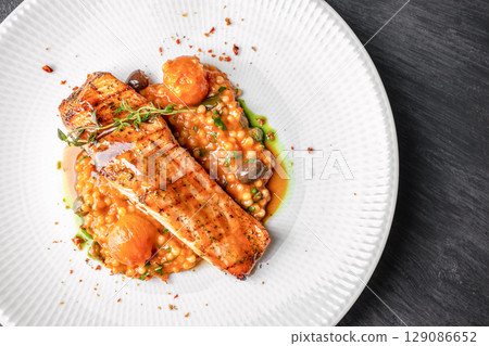 Grilled salmon fillet served on a bed of pearl couscous with cherry tomatoes, herbs, and savory sauce. top view. copy space Grilled salmon fillet served on a bed of pearl couscous with cherry tomatoes, herbs, and savory sauce. top view. copy space 129086652