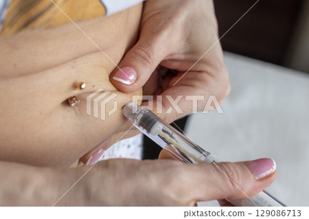 Close up shot of the woman with beautiful hands, preparing hormone medicine and injecting herself to the abdomen with pierced bellybutton. Close up shot of the woman with beautiful hands, preparing hormone medicine and injecting herself to the abdomen with pierced bellybutton. 129086713