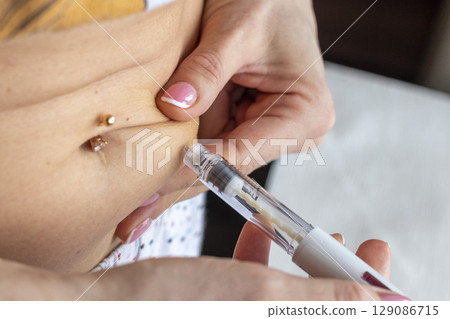 Close up shot of the woman with beautiful hands, preparing hormone medicine and injecting herself to the abdomen with pierced bellybutton. 129086715