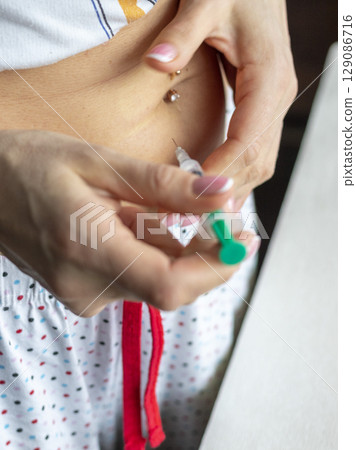 Close up shot of the woman with beautiful hands, preparing hormone medicine and injecting herself to the abdomen with pierced bellybutton. 129086716