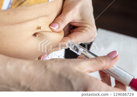 Close up shot of the woman with beautiful hands, preparing hormone medicine and injecting herself to the abdomen with pierced bellybutton. Close up shot of the woman with beautiful hands, preparing hormone medicine and injecting herself to the abdomen with pierced bellybutton. 129086729