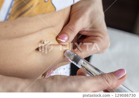 Close up shot of the woman with beautiful hands, preparing hormone medicine and injecting herself to the abdomen with pierced bellybutton. Close up shot of the woman with beautiful hands, preparing hormone medicine and injecting herself to the abdomen with pierced bellybutton. 129086730