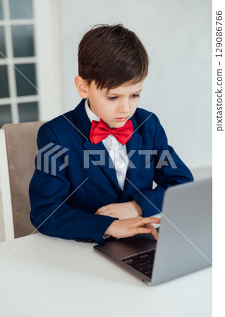 Schoolboy in Jacket Sitting At Table With Educational Laptop Schoolboy in Jacket Sitting At Table With Educational Laptop 129086766
