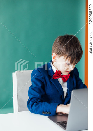Schoolboy in Jacket Sitting At Table With Educational Laptop Schoolboy in Jacket Sitting At Table With Educational Laptop 129086769