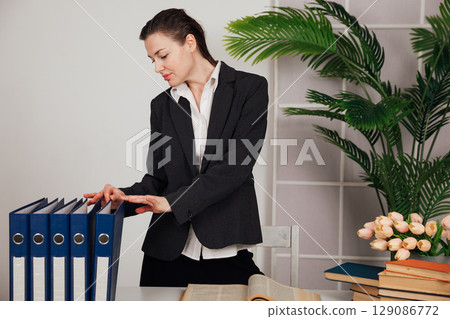 Woman in business suit sitting at desk with folders and books 129086772
