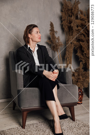 Woman in business suit sitting on vintage chair in gray room 129086773