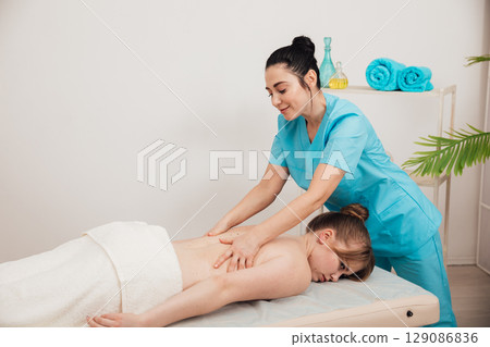 Massage therapist doing medical back and body massage to woman 129086836