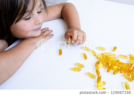 Caucasian young girl examining yellow capsules on white table 129087198