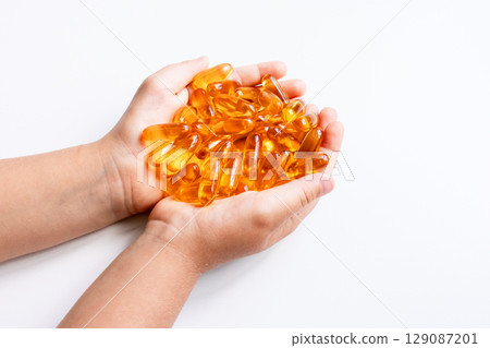 Close up of child hands holding omega 3 fish oil capsules on white background 129087201