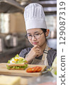 Thoughtful Young Asian Female Chef Evaluating Sandwich in Commercial Kitchen 129087319