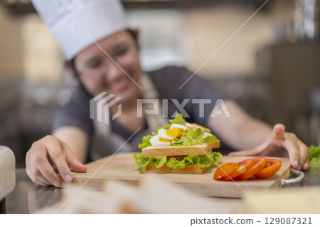 Smiling Young Asian Female Chef Making Sandwich 129087321